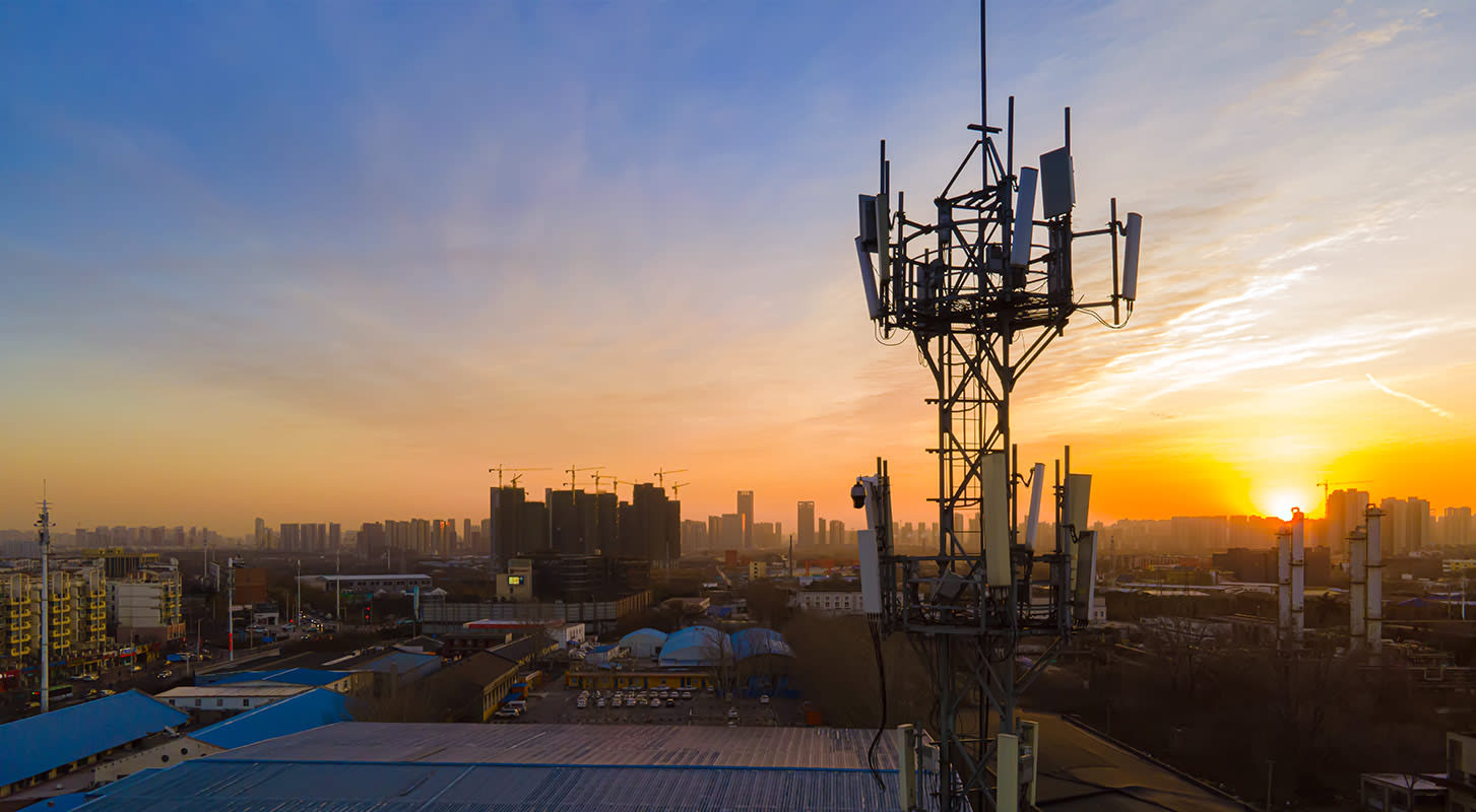 A cell phone tower stands tall at sunset in India, surrounded by a colorful sky filled with orange and purple tones.